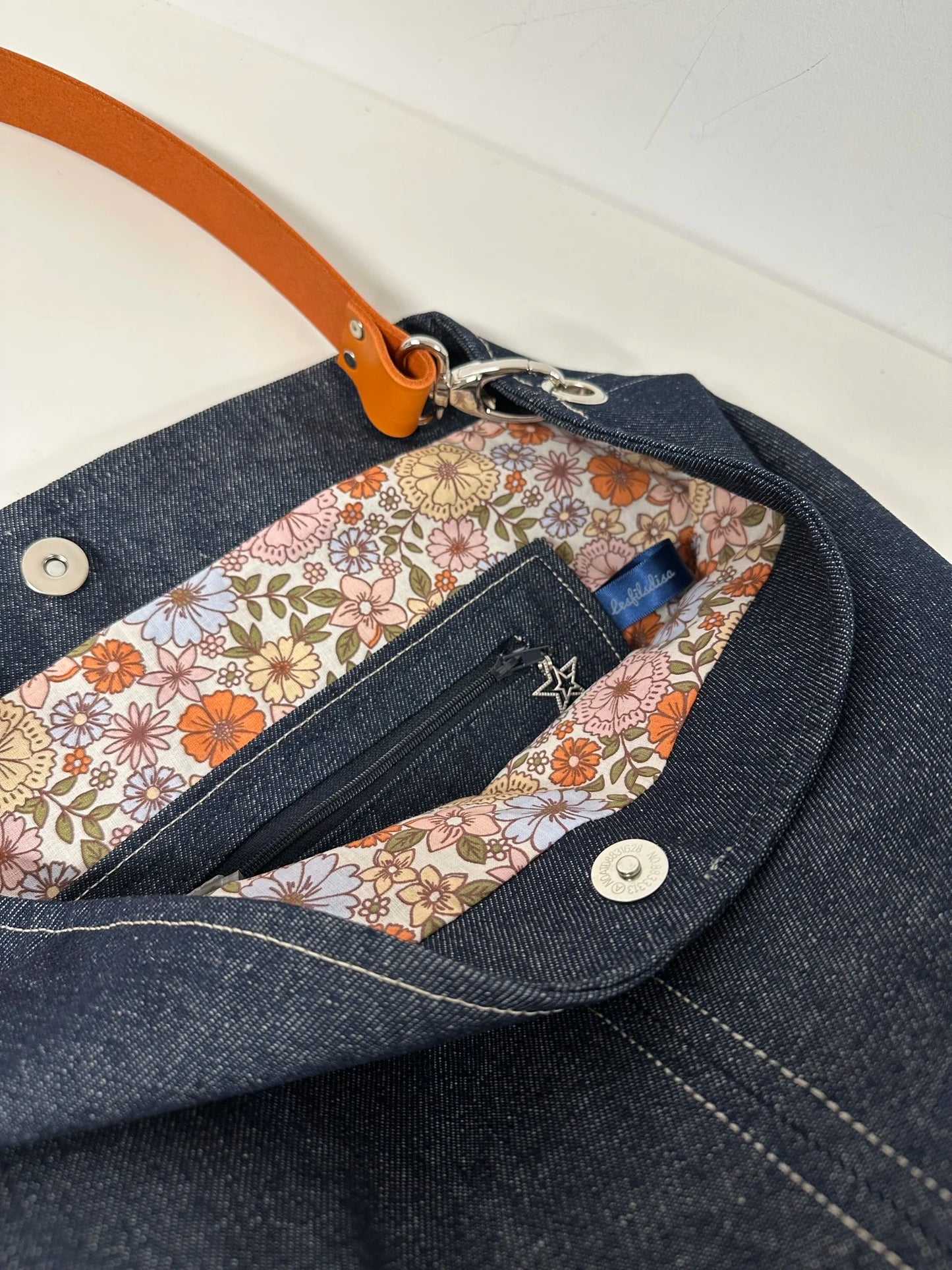 La poche zippée du sac hobo en denim et son anse en cuir orange .