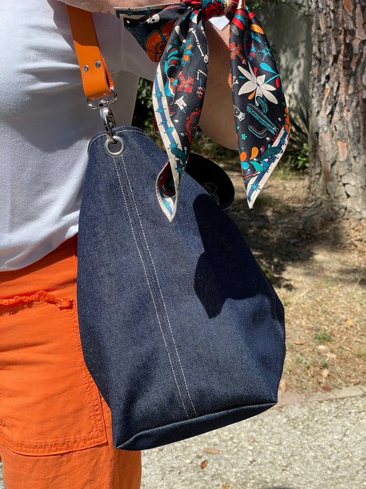 Le sac hobo en denim et son anse en cuir orange porté à 'épaule.