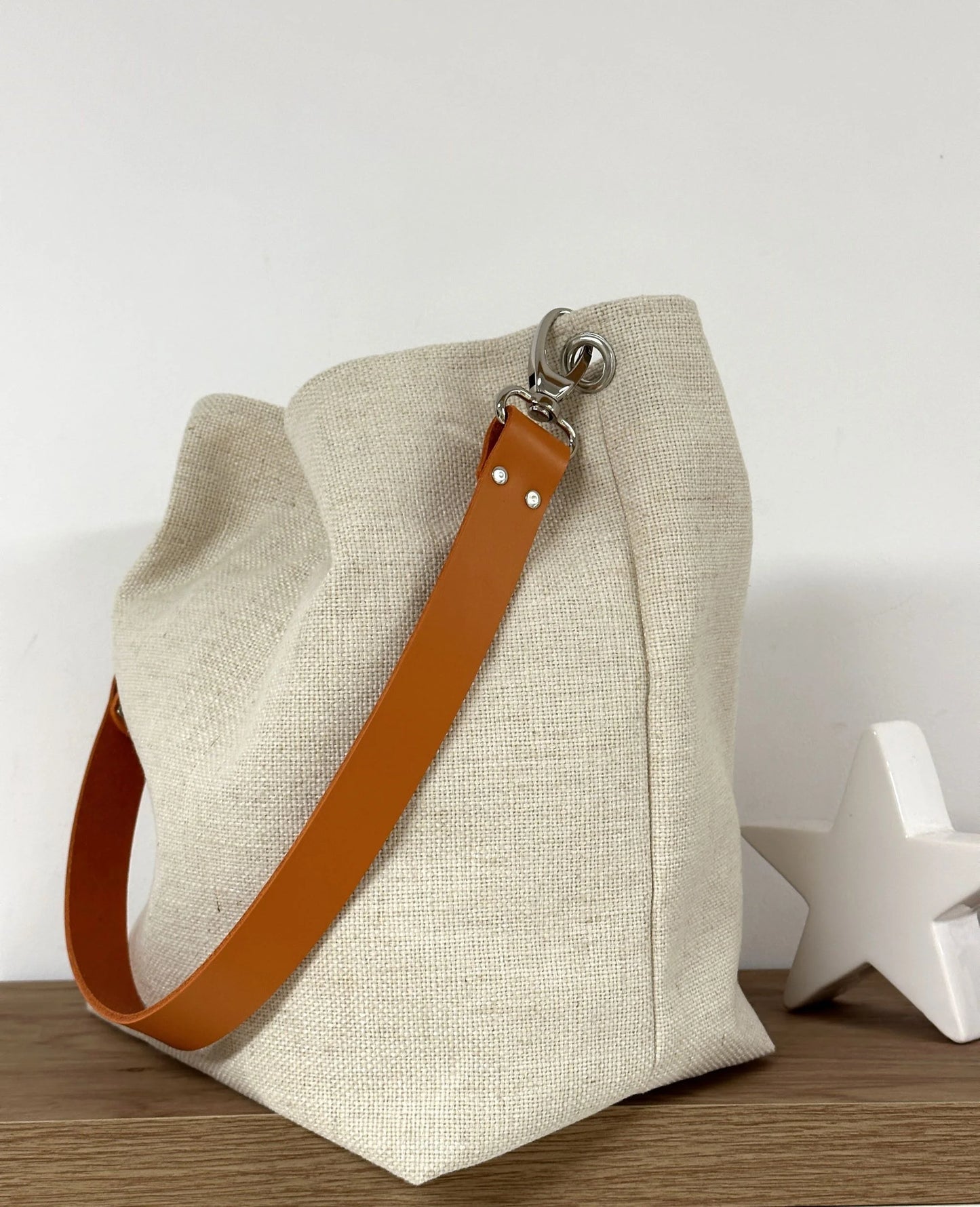 sac hobo en lin ivoire et son anse en cuir orange, posé.