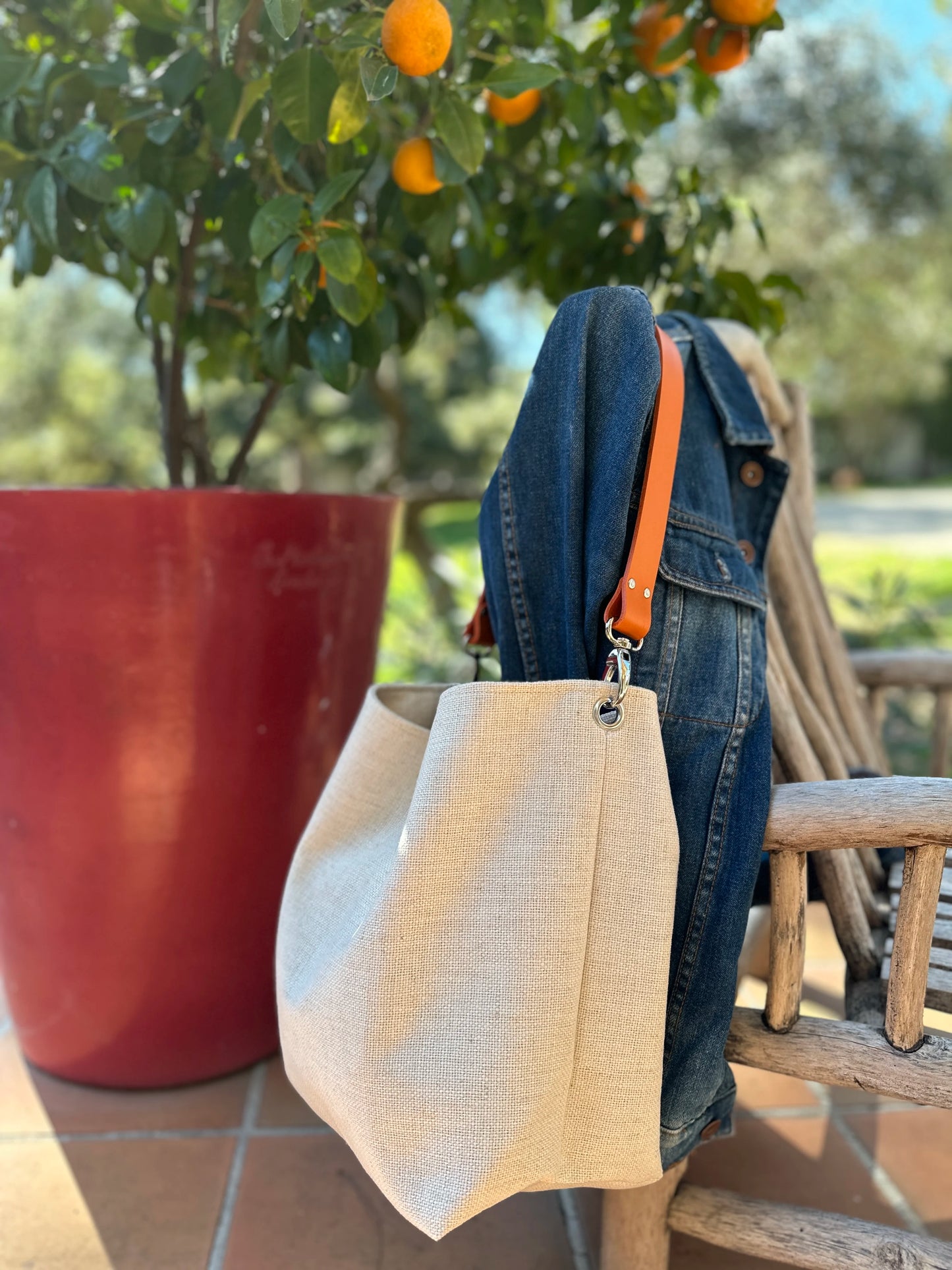 Le sac hobo en lin ivoire et son anse en cuir orange, accroché sur un fauteuil.