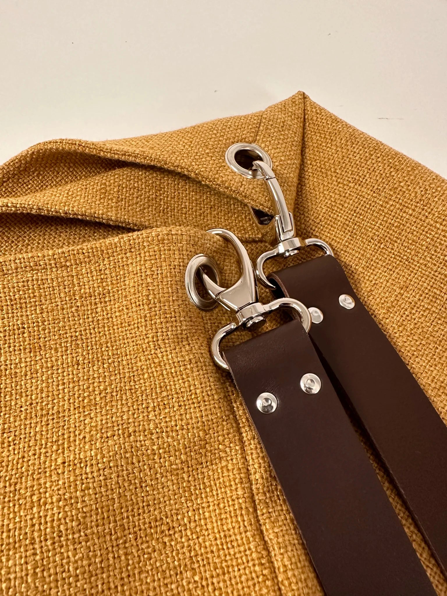 Vue de détail de l'anse en cuir marron du sac hobo en lin jaune moutarde .