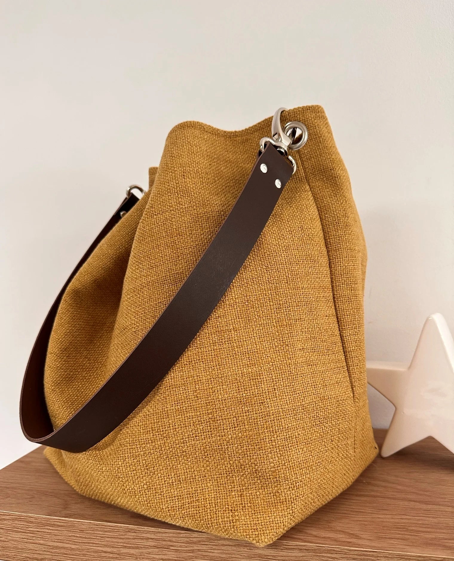 Le sac hobo en lin jaune moutarde et son anse en cuir marron amovible.