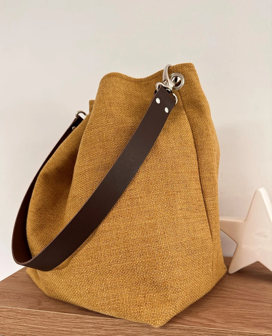 Le sac hobo en lin jaune moutarde et son anse en cuir marron amovible.
