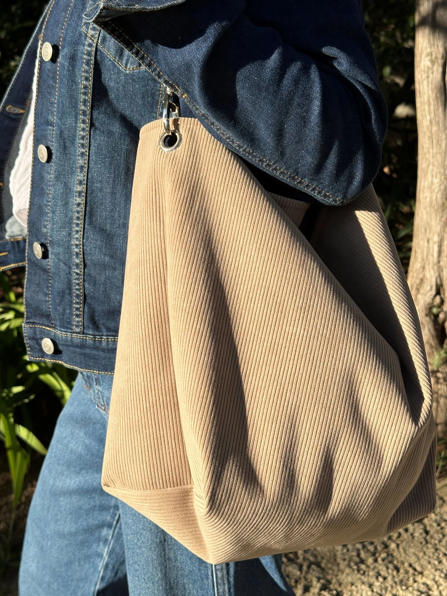 Le sac Hobo en velours côtelé beige, porté à l'épaule.