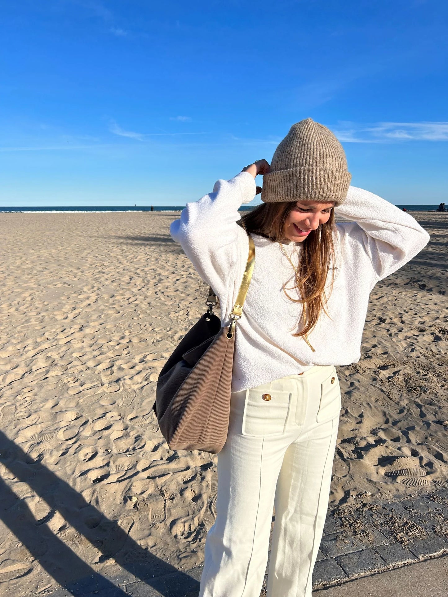 Le sac hobo en velours cotelé marron chamois et son anse en cuir doré, porté à l'épaule.