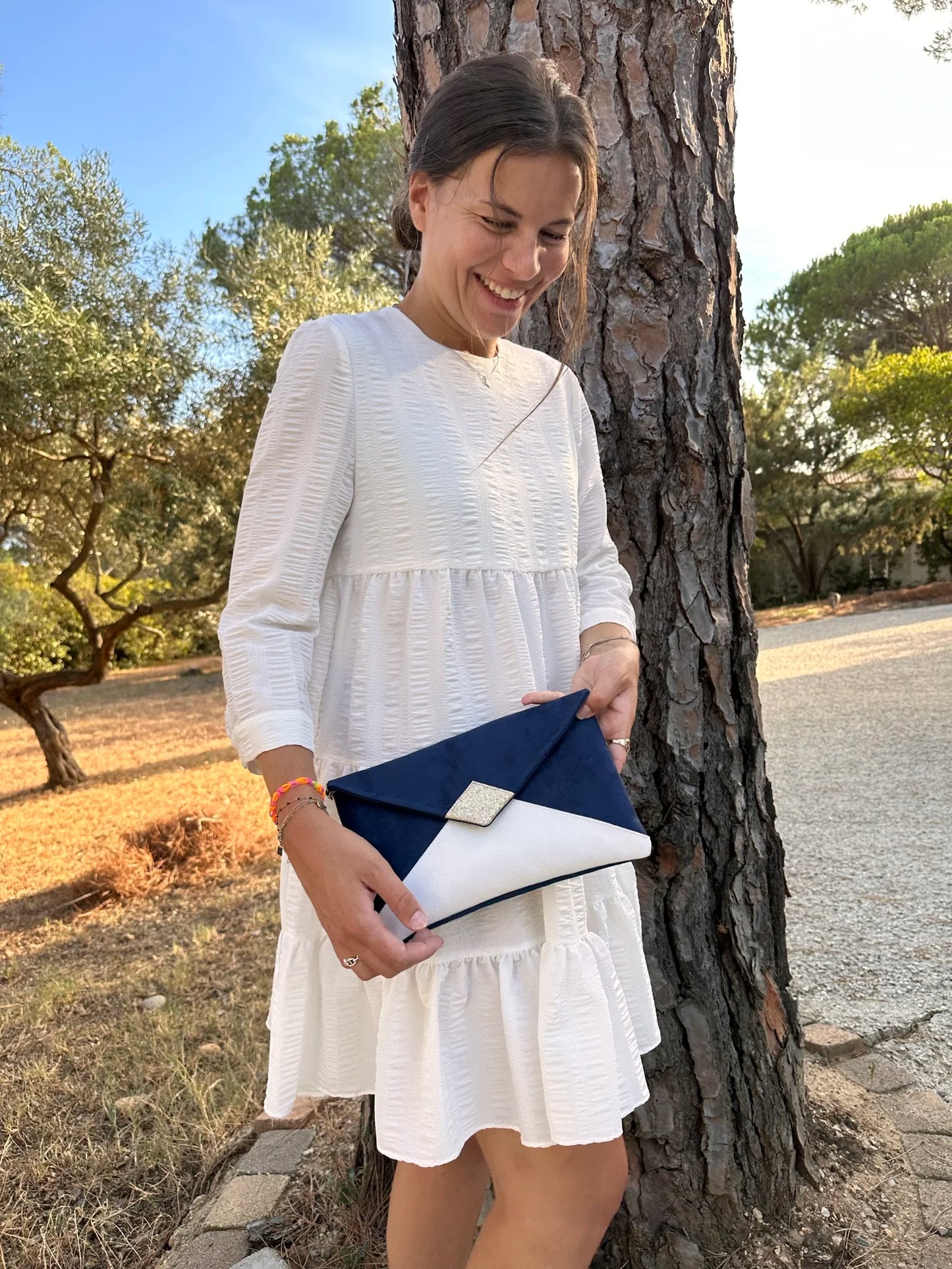Jeune femme qui porte le sac pochette Isa bleu marine et blanc à paillettes dorées.