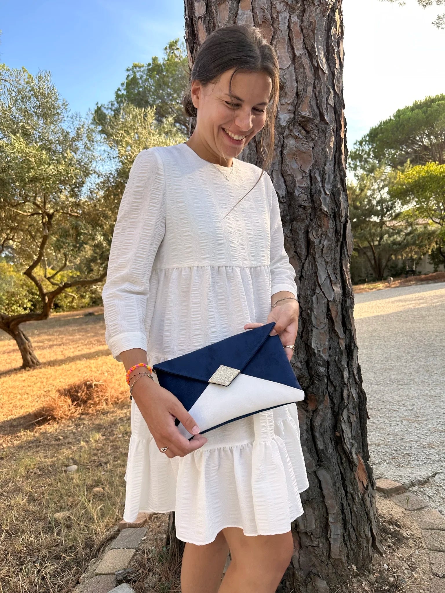 Jeune femme qui porte le sac pochette Isa bleu marine et blanc à paillettes dorées.