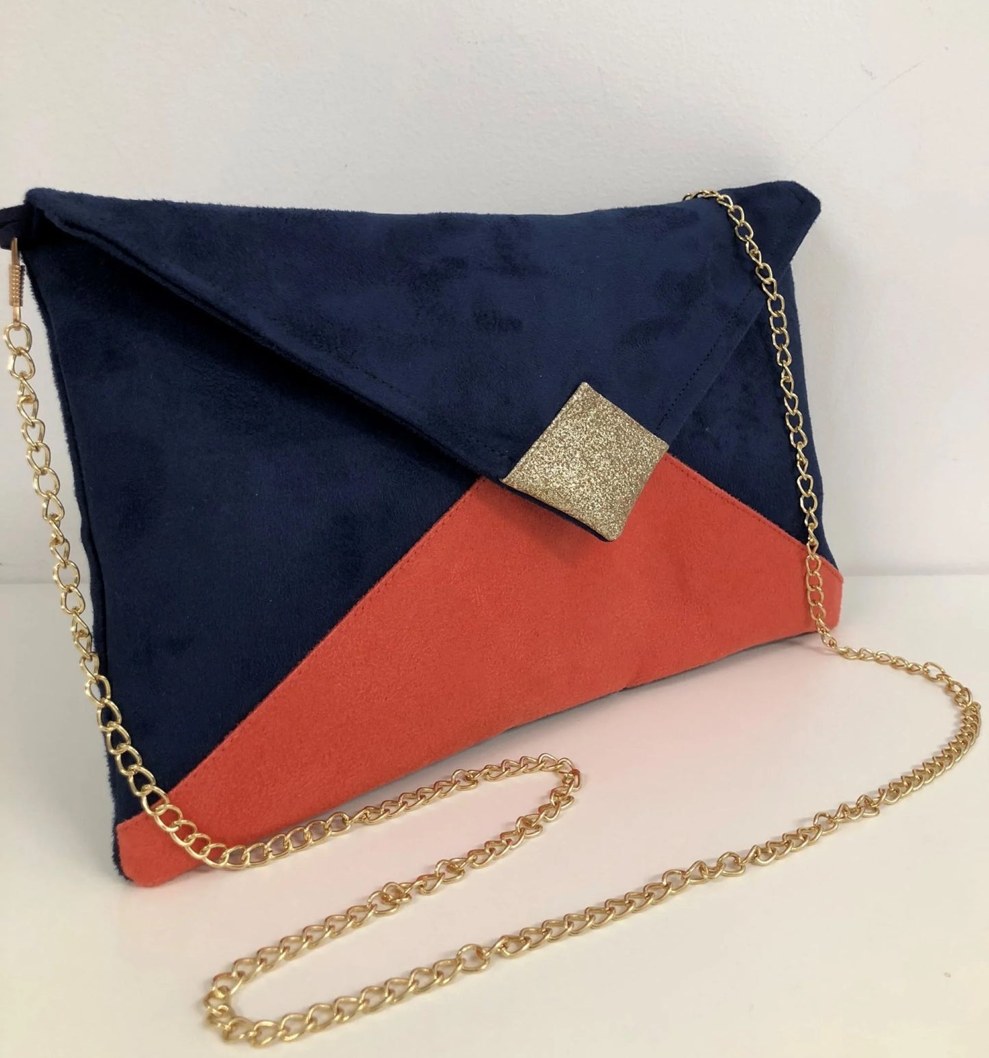 Le sac pochette Isa bleu marine et corail à paillettes dorées avec chainette amovible.