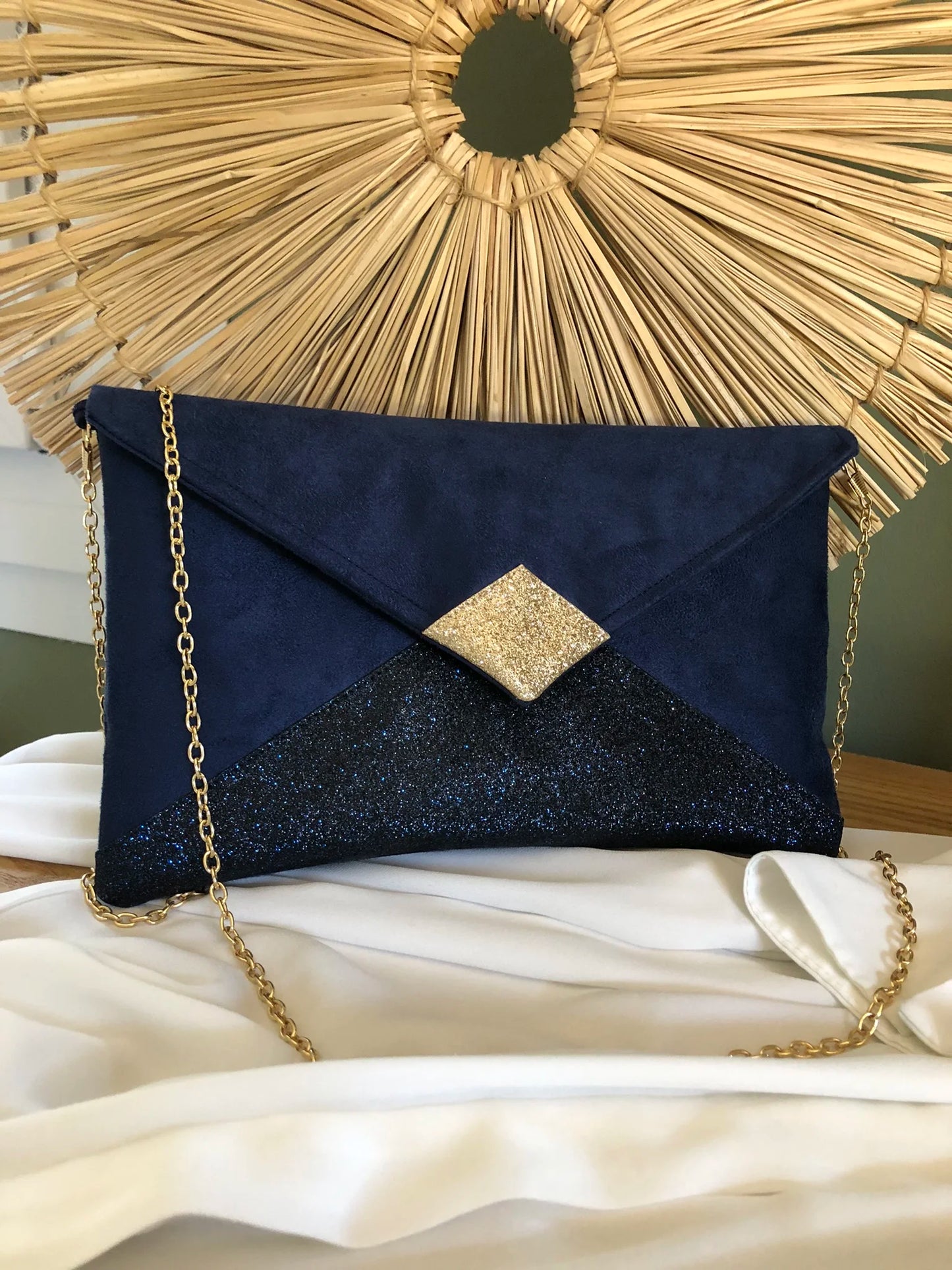Le sac pochette Isa bleu marine et doré à paillettes, avec chainette amovible, posé sur chemisier.