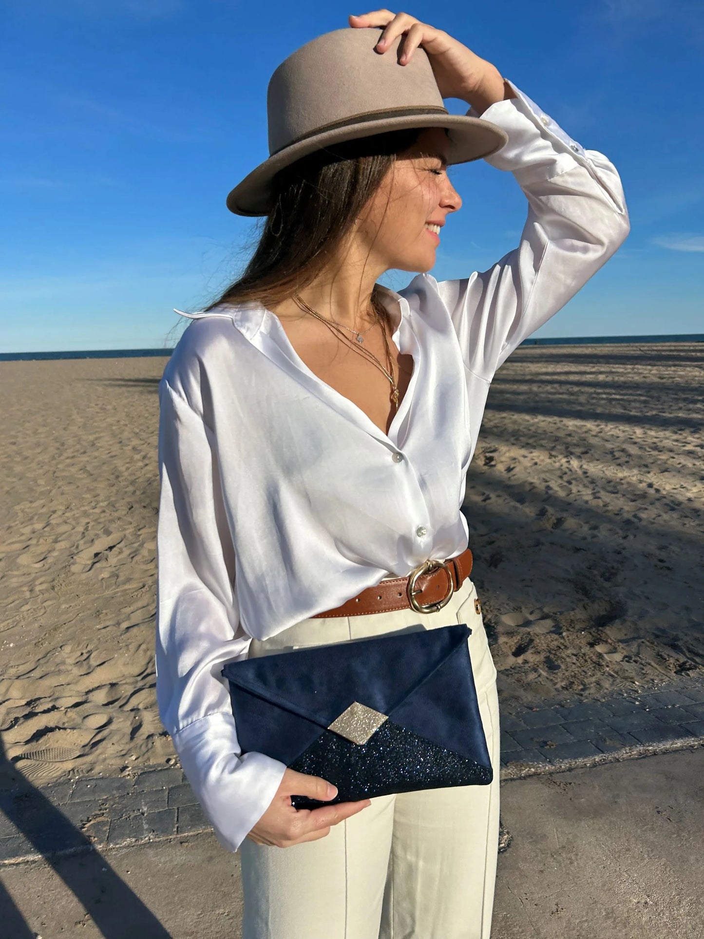 Le sac pochette Isa bleu marine et doré à paillettes, porté en main.