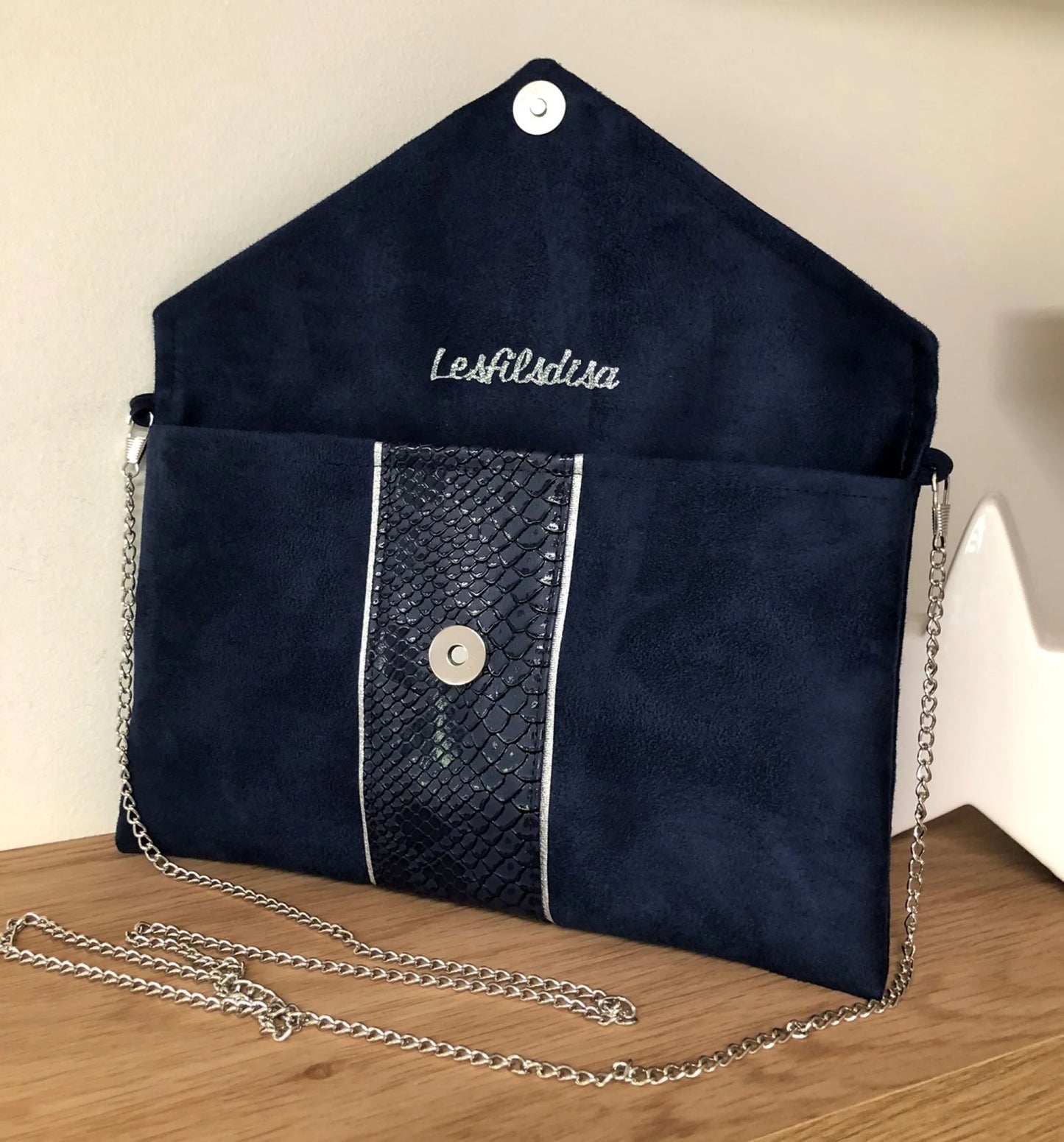 Le sac pochette Isa bleu marine reptile à liseré argenté ouvert, avec sa chainette amovible.