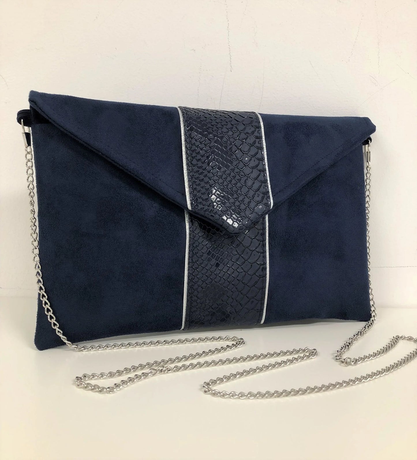 Le sac pochette Isa bleu marine reptile à liseré argenté, avec sa chainette amovible.