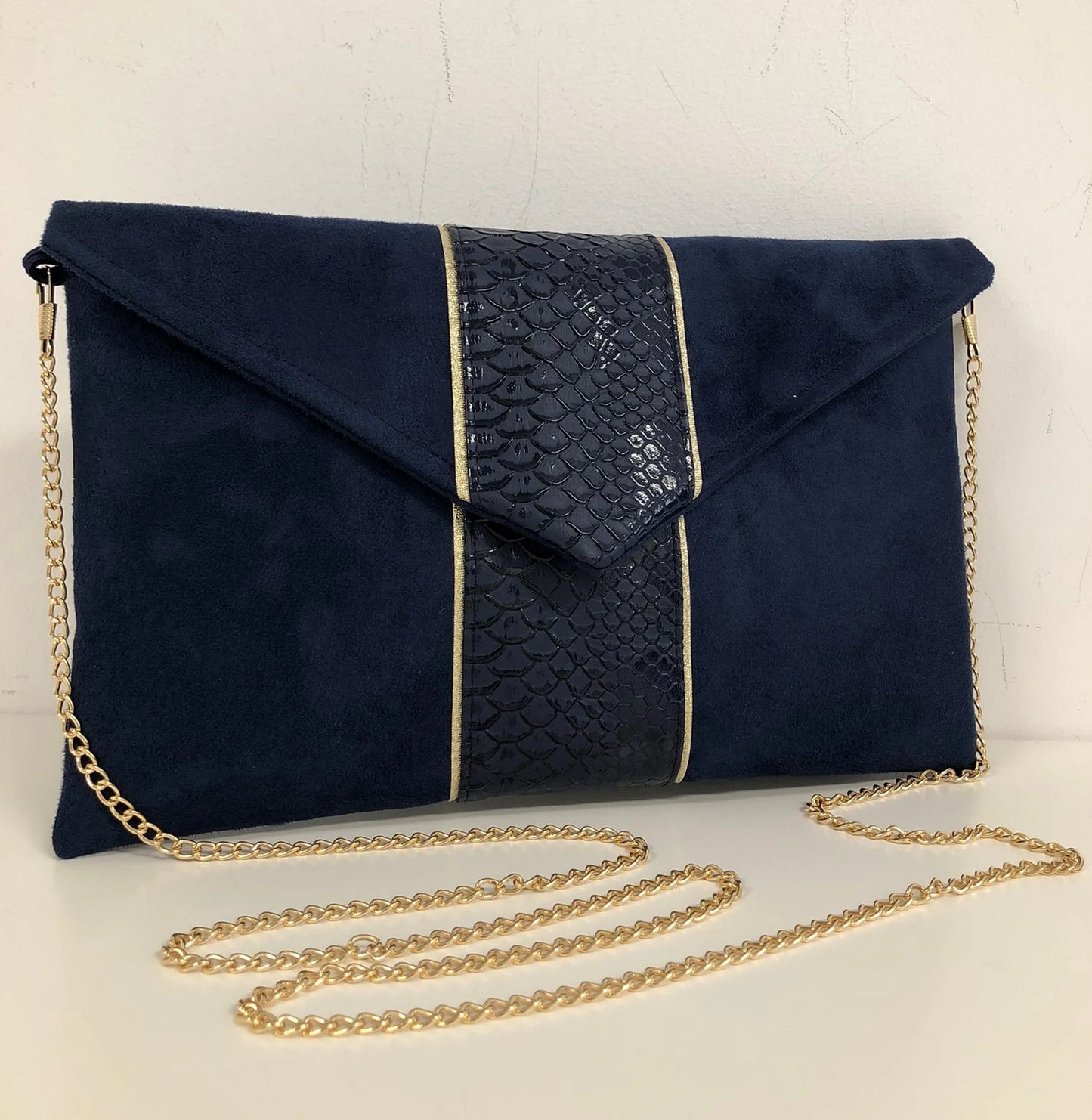 Le sac pochette Isa bleu marine reptile à liseré doré, avec chainette amovible.