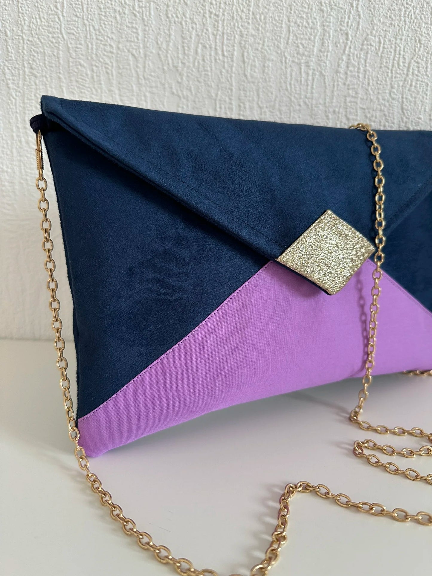 Vue latérale du sac pochette Isa bleu marine violet et doré avec sa chainette dorée amovible.