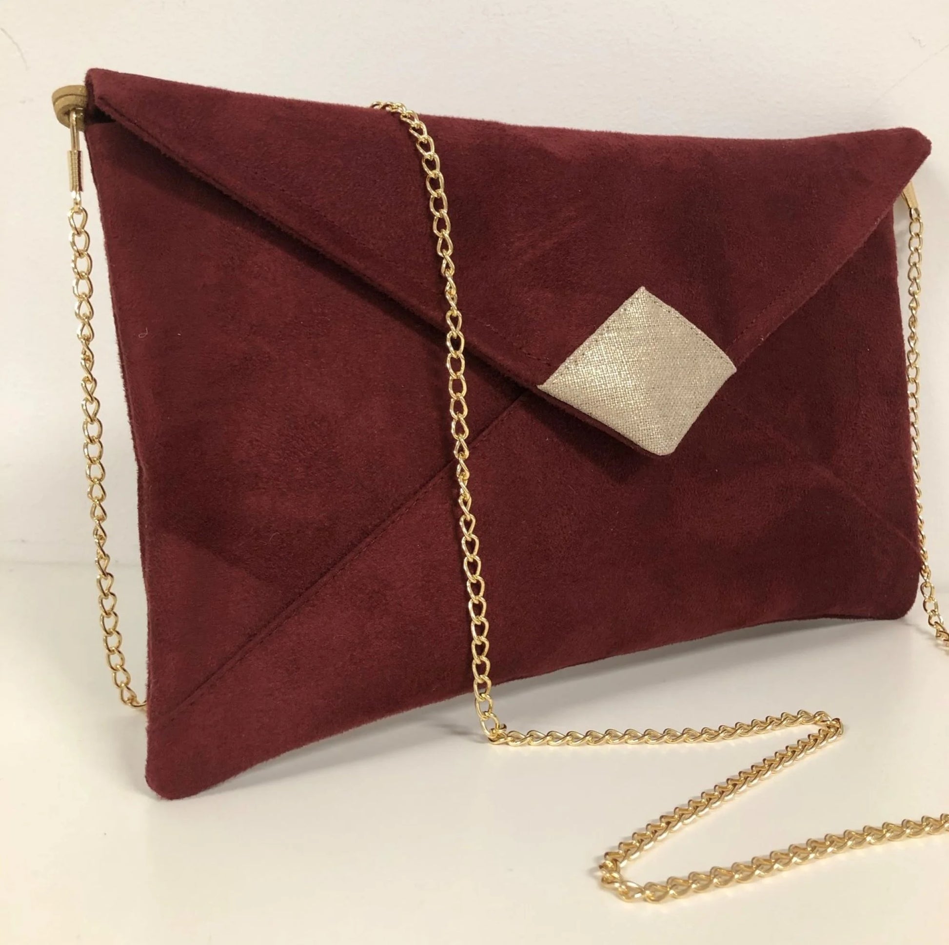 Le sac pochette Isa bordeaux et lin doré, avec chainette amovible, sur fond neutre.