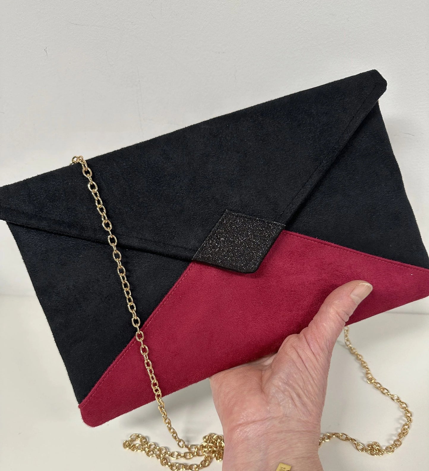 Le sac pochette Isa noir et fuchsia à paillettes porté à la main.