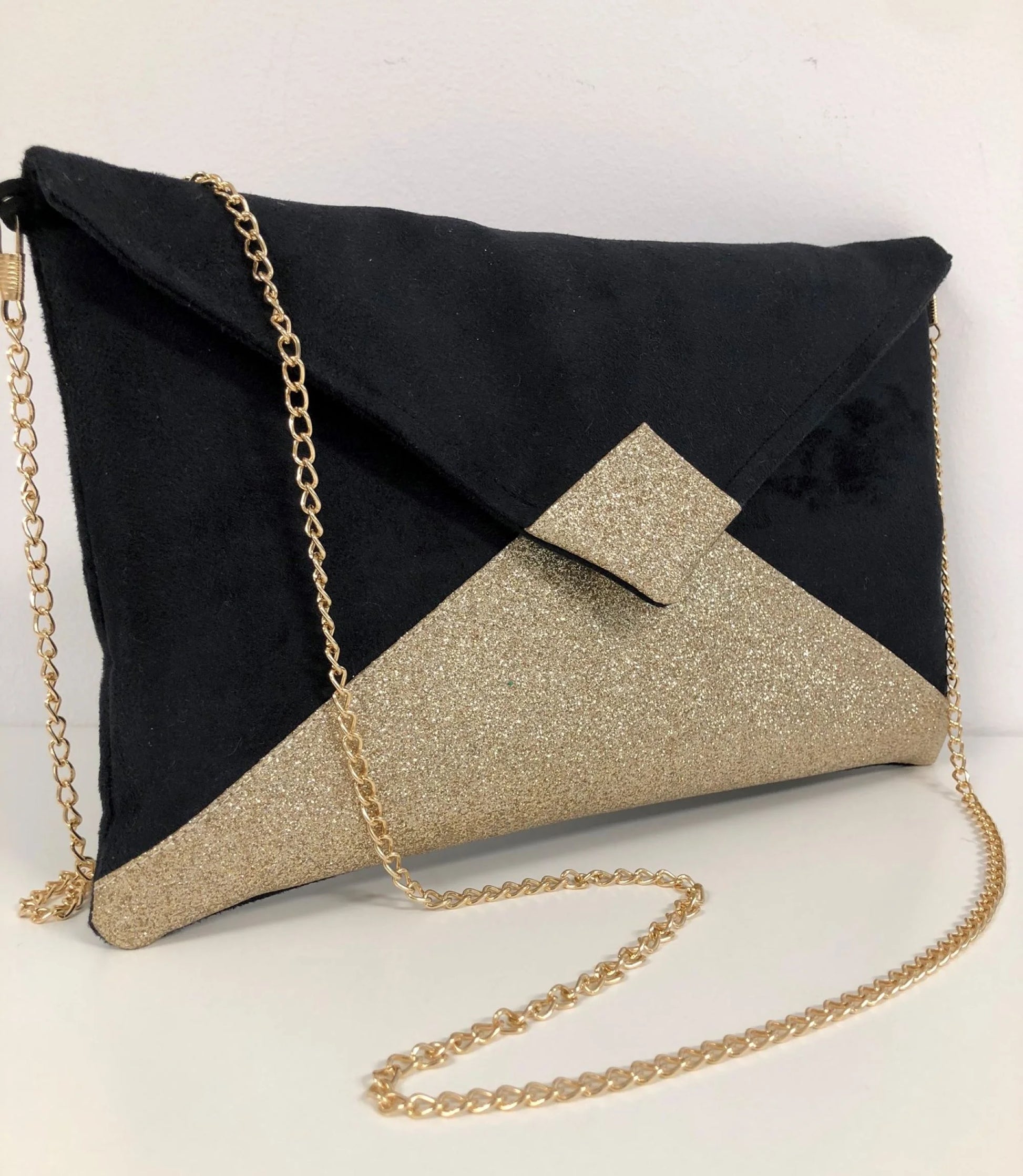Le sac pochette Isa noir à paillettes dorées, avec chainette dorée amovible.