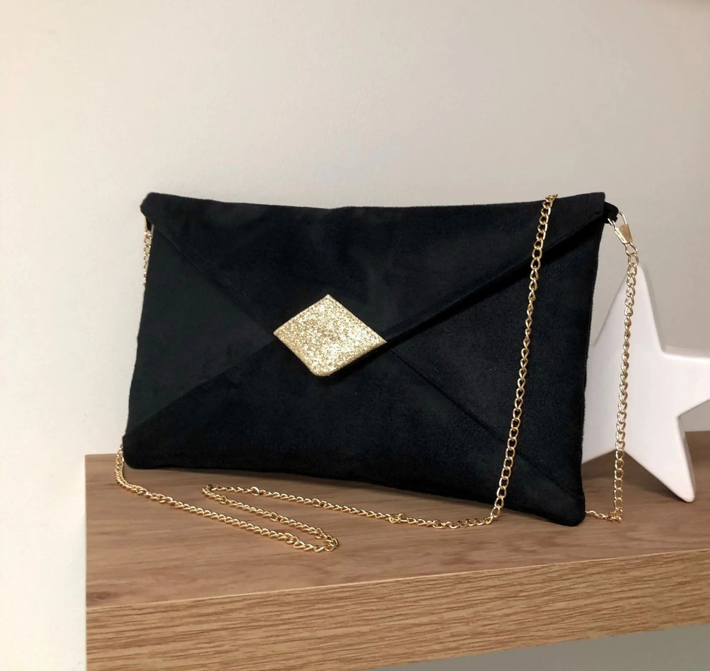 Le sac pochette Isa en suédine noire et paillettes dorées, avec chainette dorée amovible.
