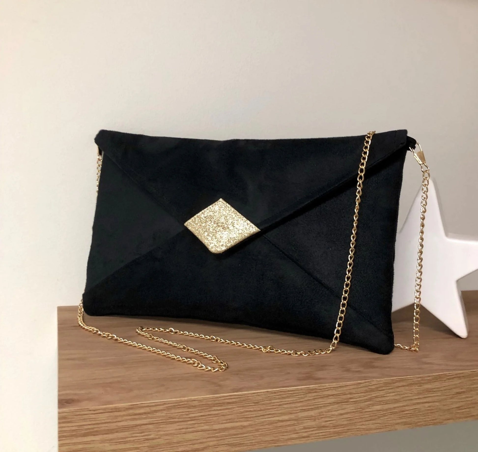 Le sac pochette Isa en suédine noire et paillettes dorées, avec chainette dorée amovible.