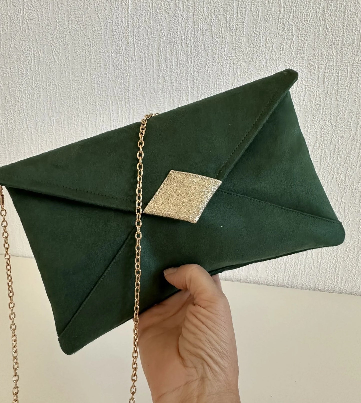 Le sac pochette Isa vert sapin et paillettes dorées tenu en main.