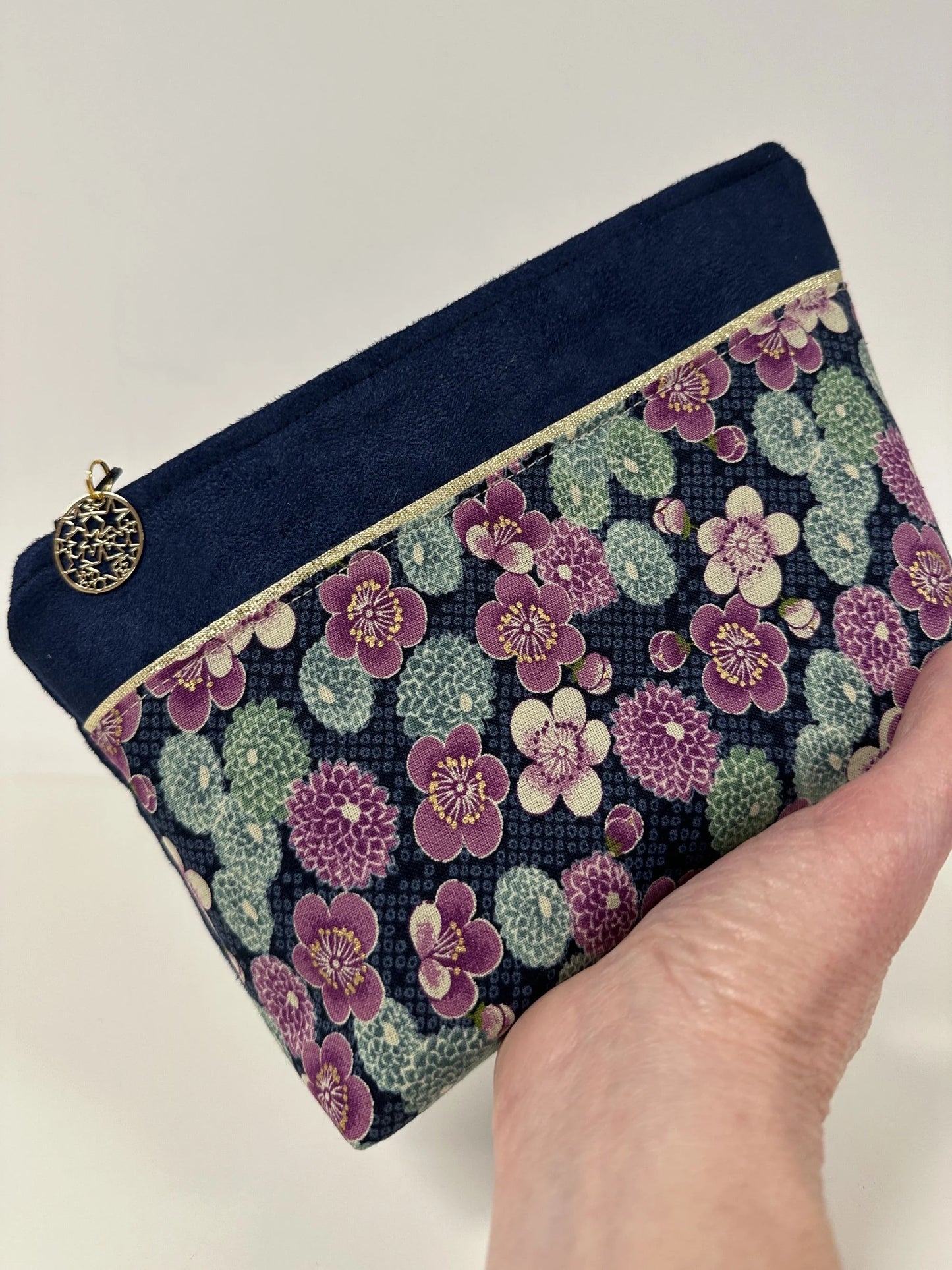 La trousse à maquilage bleu marine en tissu japonais à fleurs mauves, portée à la main.