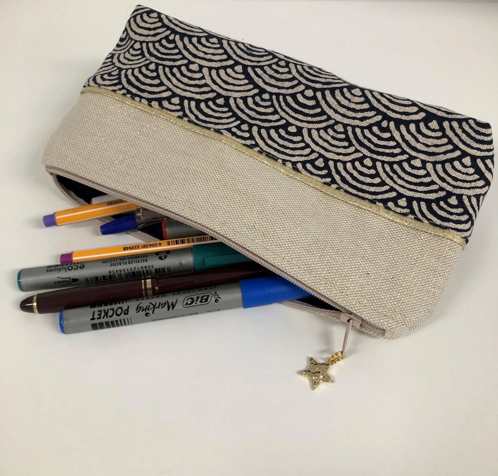 La trousse à stylos en tissu japonais bleu nuit et doré, contenant plein de crayons.