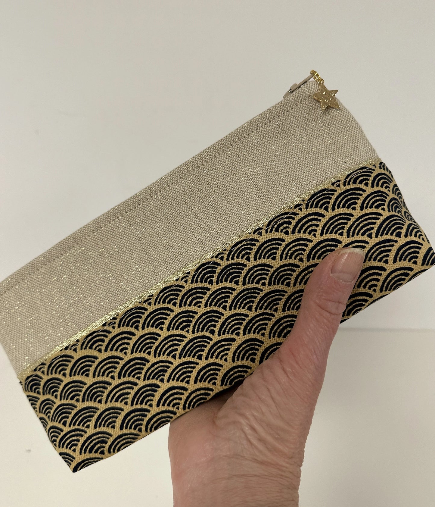 La trousse à stylos en tissu japonais Seigaiha bleu marine et doré, tenue dans la main.
