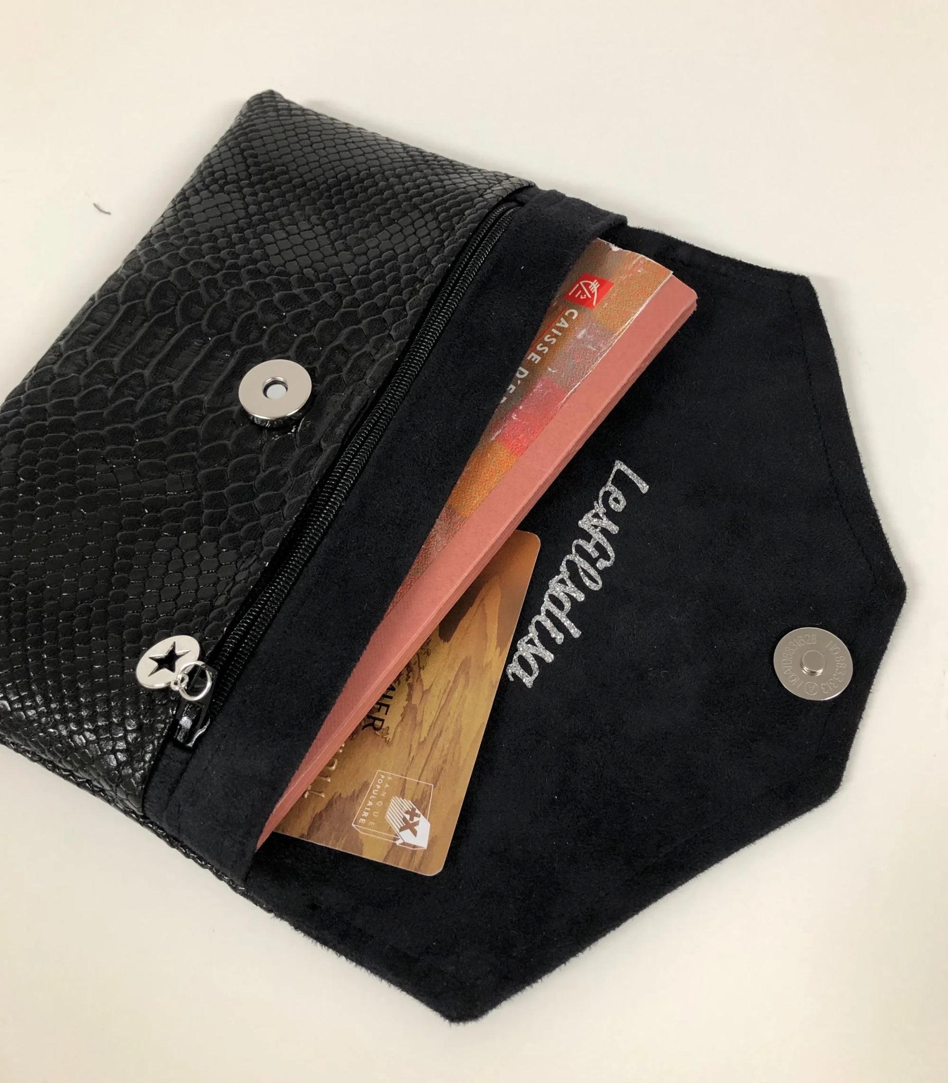 Le compagnon de sac noir aspect reptile qui contient le carnet de chèques, la carte bancaire.