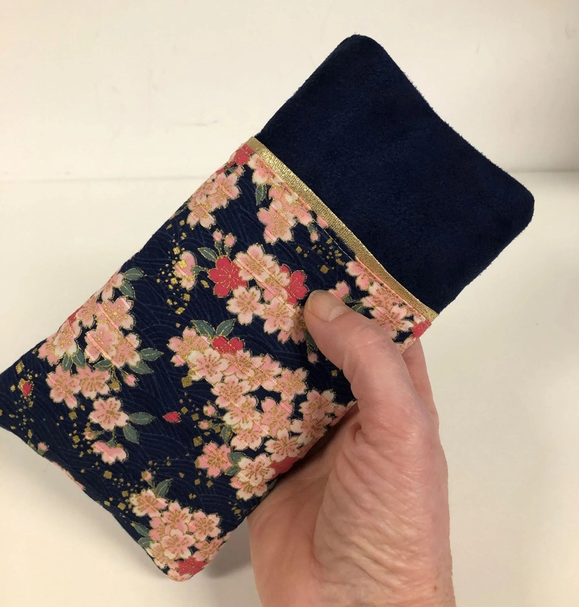 L'étui à lunettes bleu marine en tissu japonais à fleurs de cerisier, tenu en main.