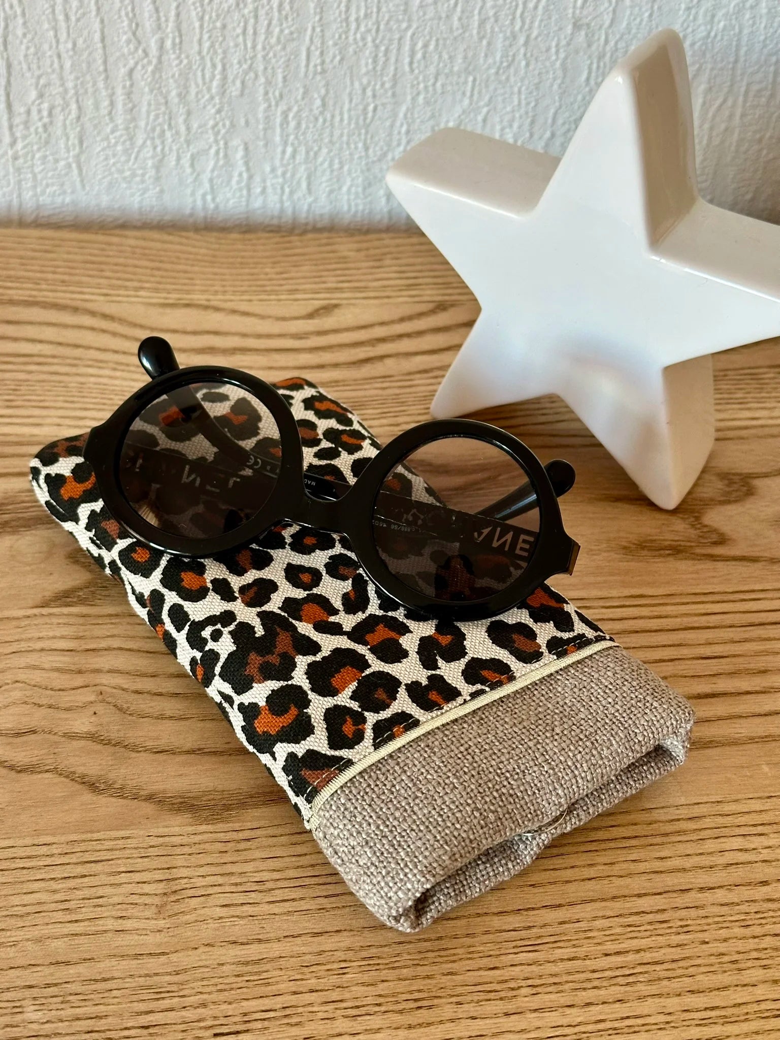 L'étui à lunettes léopard en lin beige, présenté avec des lunettes de soleil.