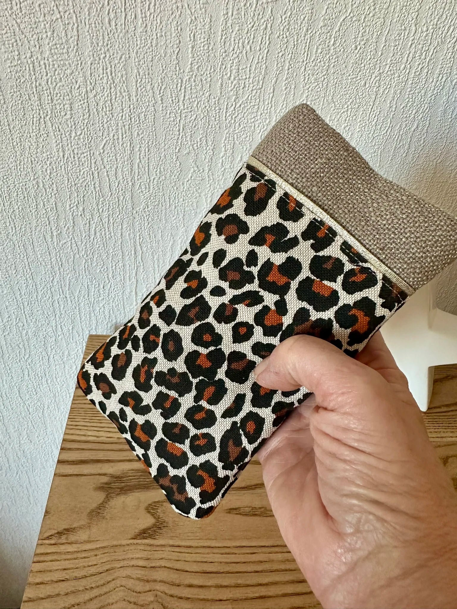 L'étui à lunettes léopard en lin beige tenu en main.