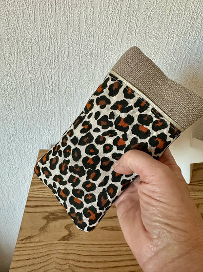 L'étui à lunettes léopard en lin beige tenu en main.
