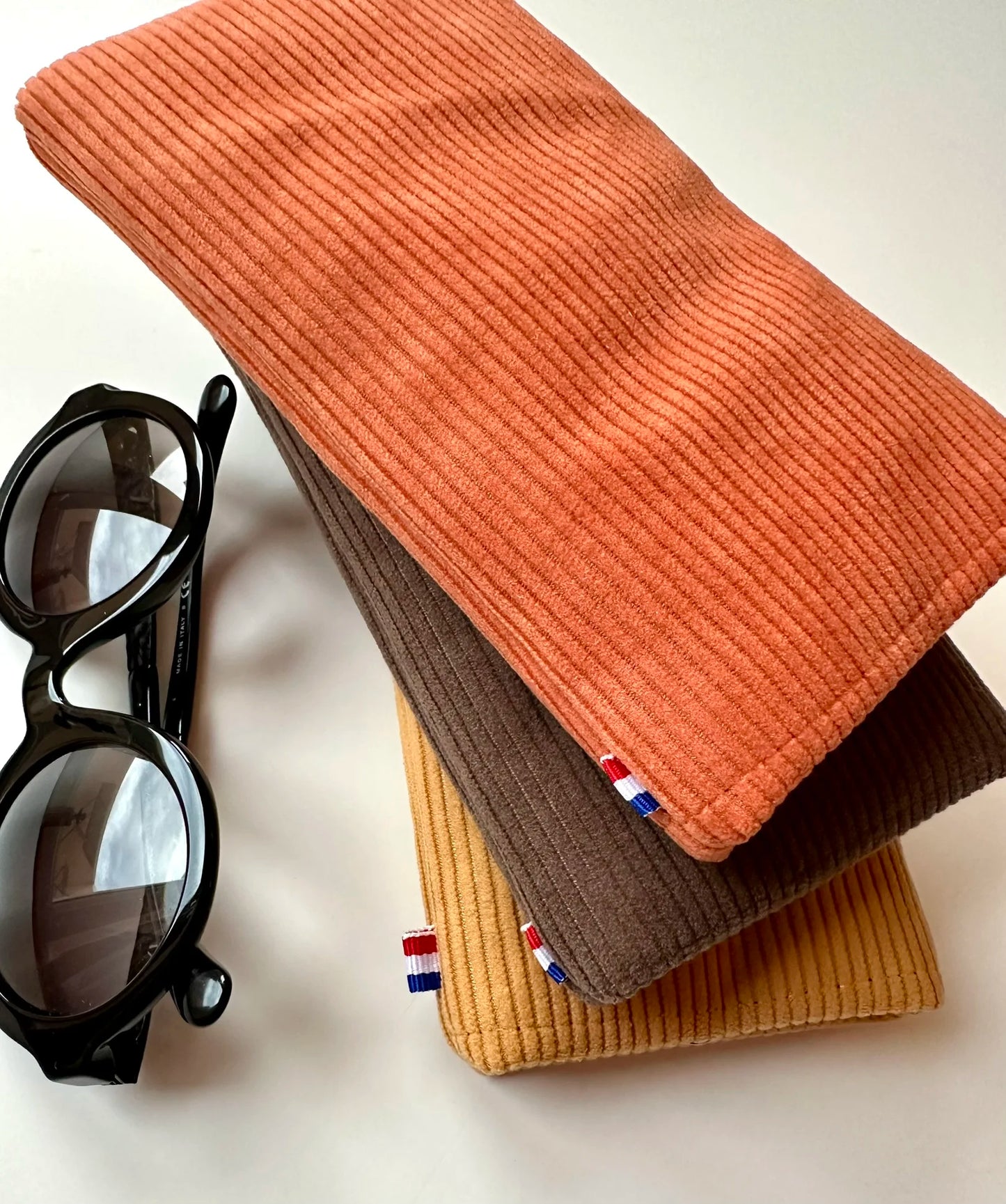 L'étui à lunettes en velours cotelé orange, posé sur le marron et le jaune moutarde.