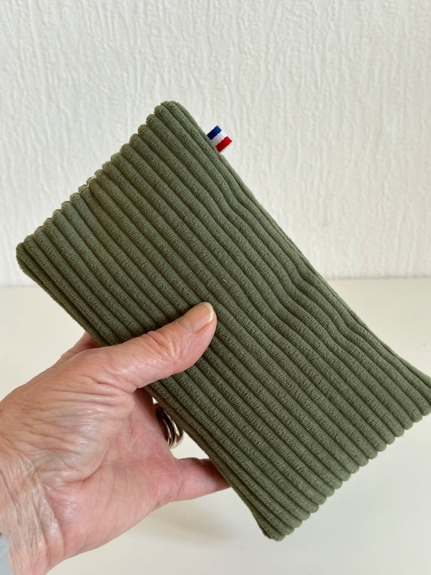 L'étui à lunettes en velours cotelé vert armée, tenu dans la main.