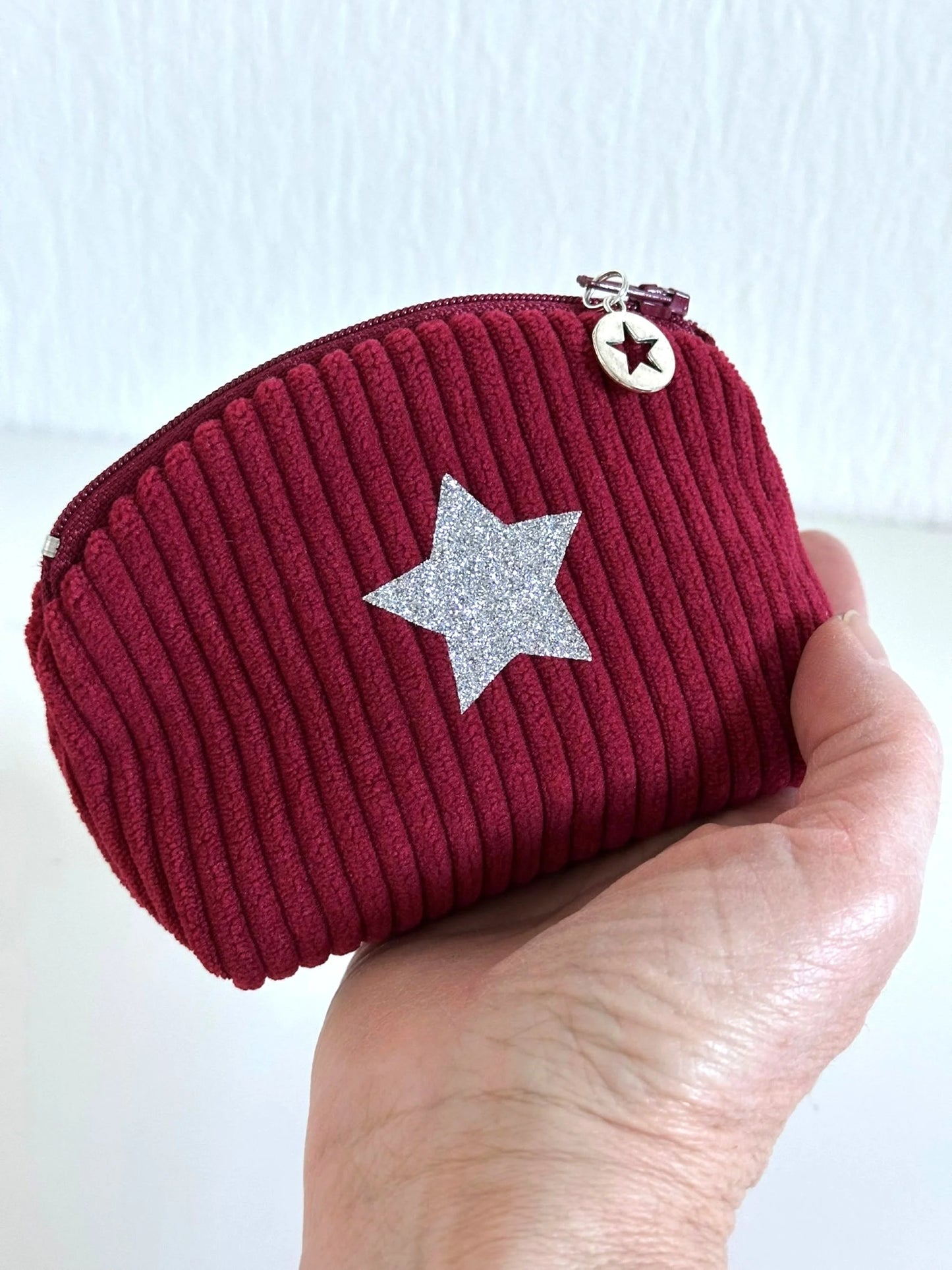 Le petit porte monnaie en velours cotelé bordeaux, tenu dans la main.