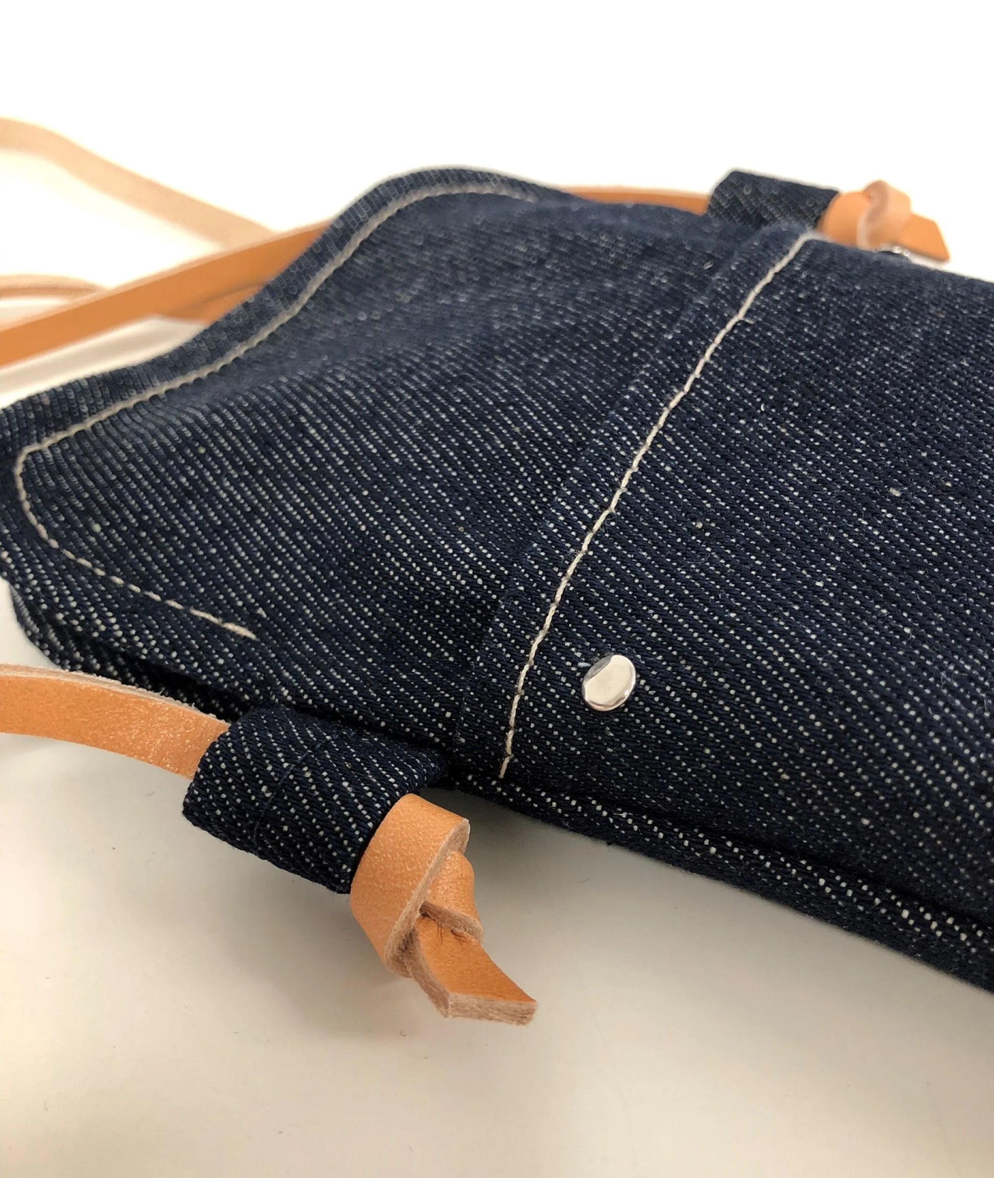 Les surpiqures de la  pochette bandoulière téléphone en denim et cuir naturel.