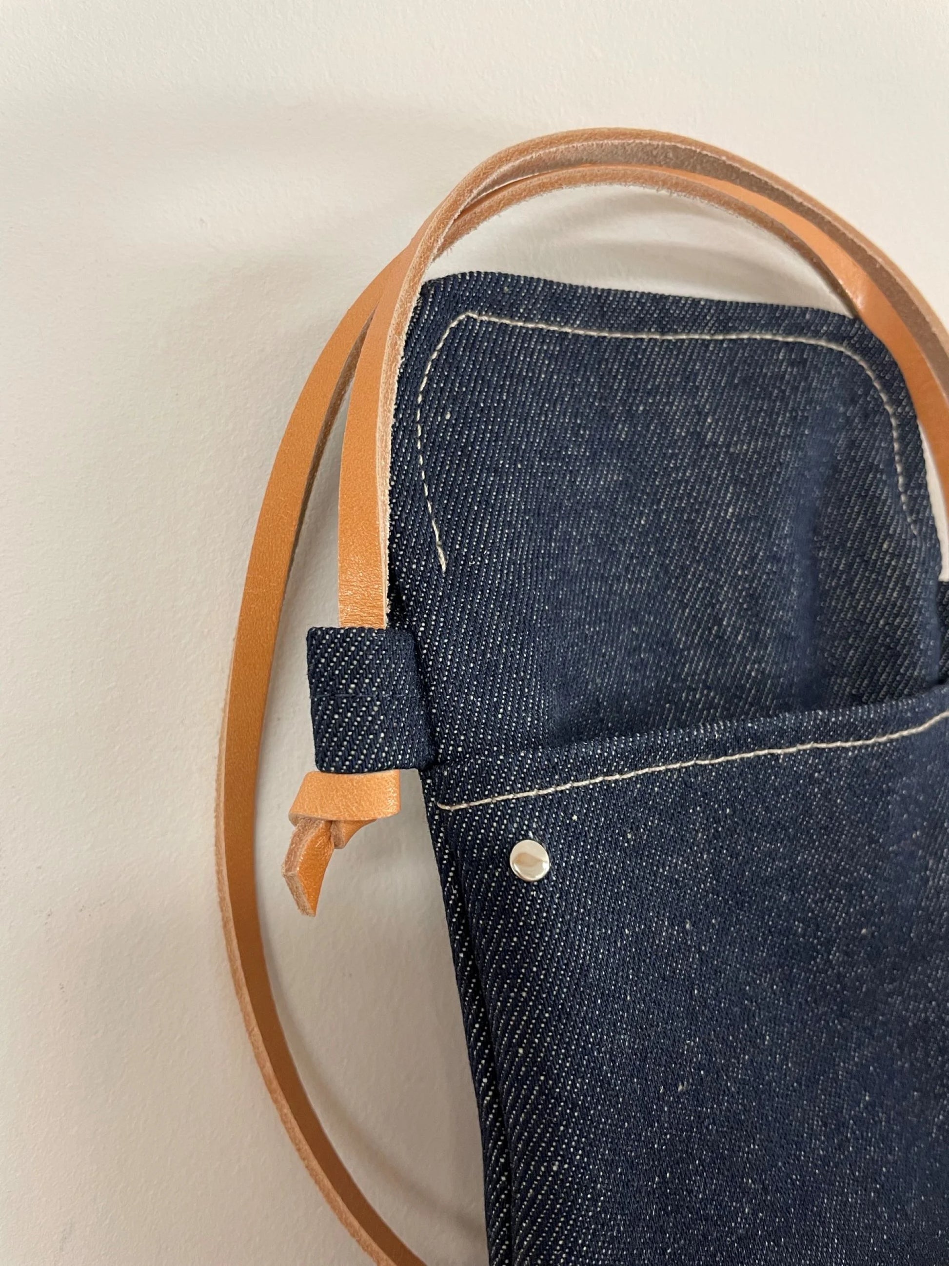 La lanière en cuir naturel nouée de la  pochette bandoulière téléphone en denim .