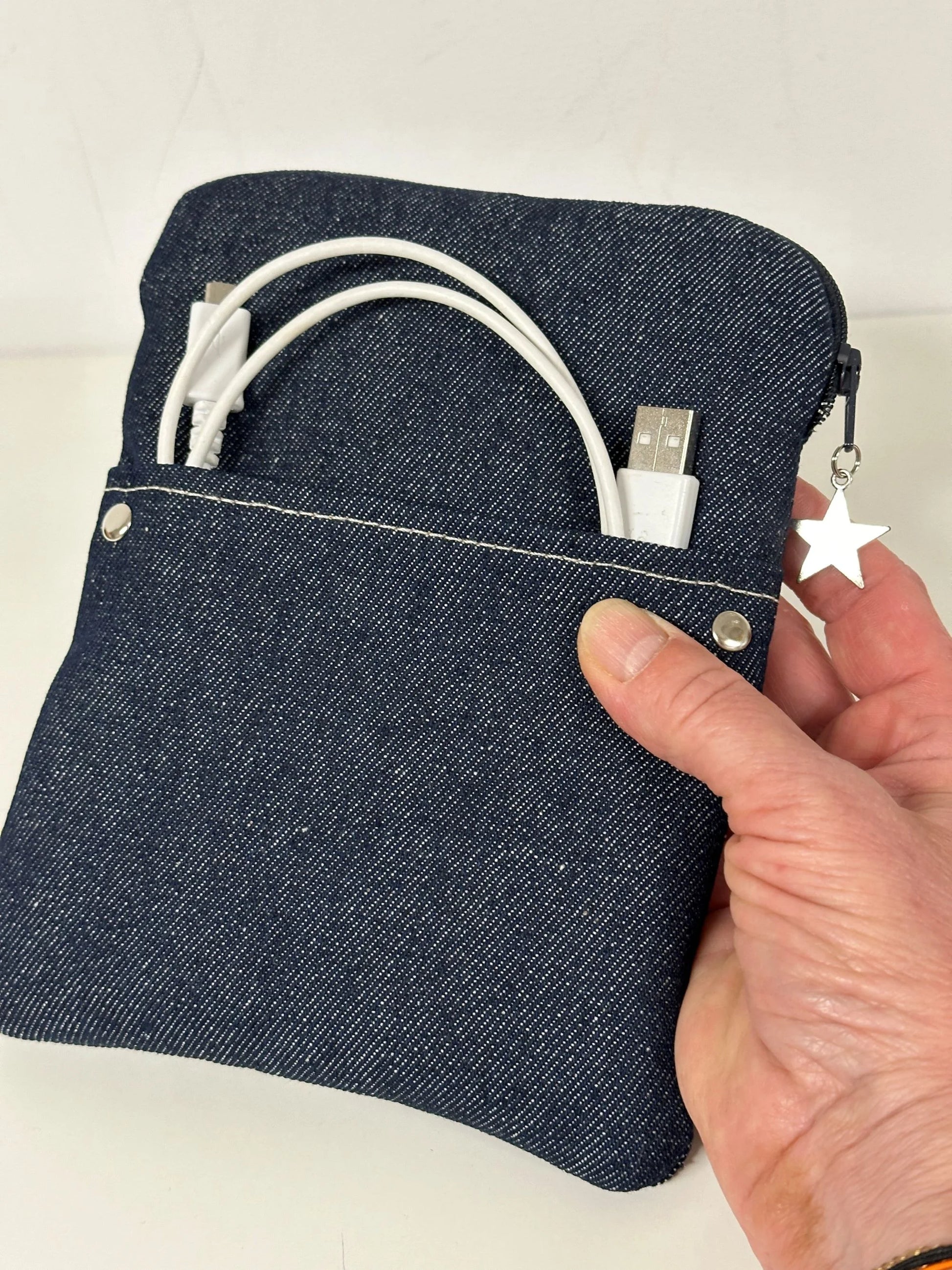 La pochette liseuse en denim brut, tenue en main.