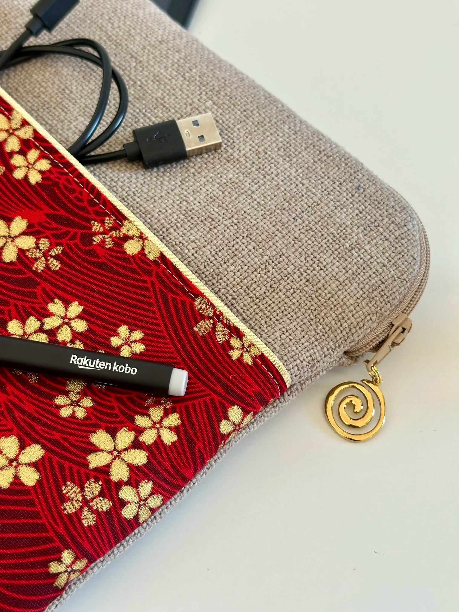 Le câble de chargement dans la poche de la pochette liseuse en lin et tissu japonais Sakura rouge et doré.
