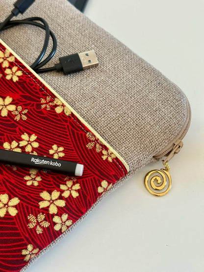 Le câble de chargement dans la poche de la pochette liseuse en lin et tissu japonais Sakura rouge et doré.