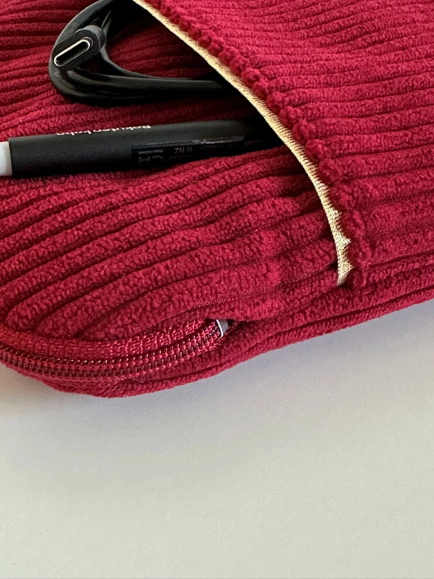 Le liseré doré de la poche avant de la pochette liseuse en velours cotelé bordeaux.