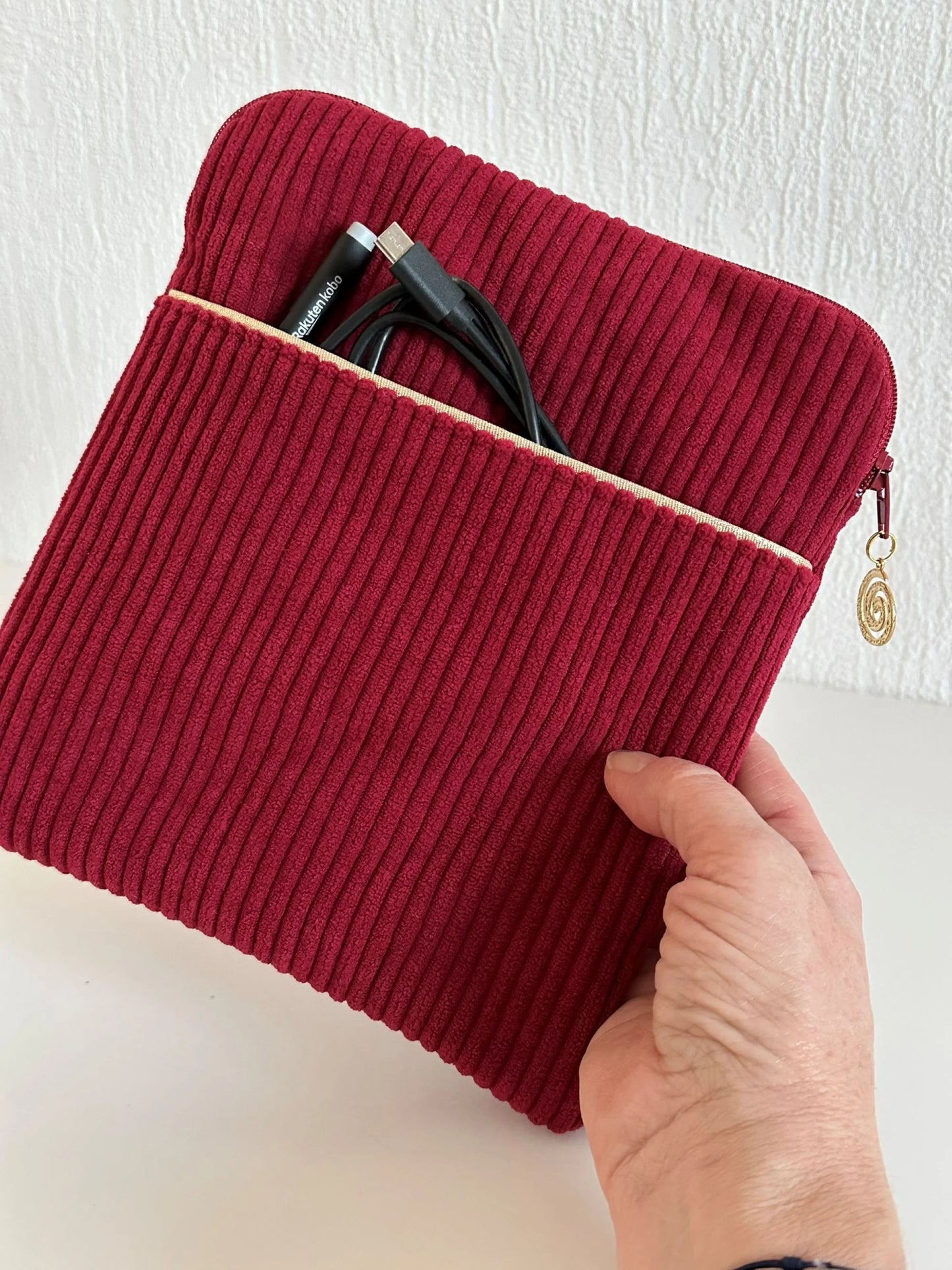 La pochette liseuse en velours cotelé bordeaux, tenue dans la main.