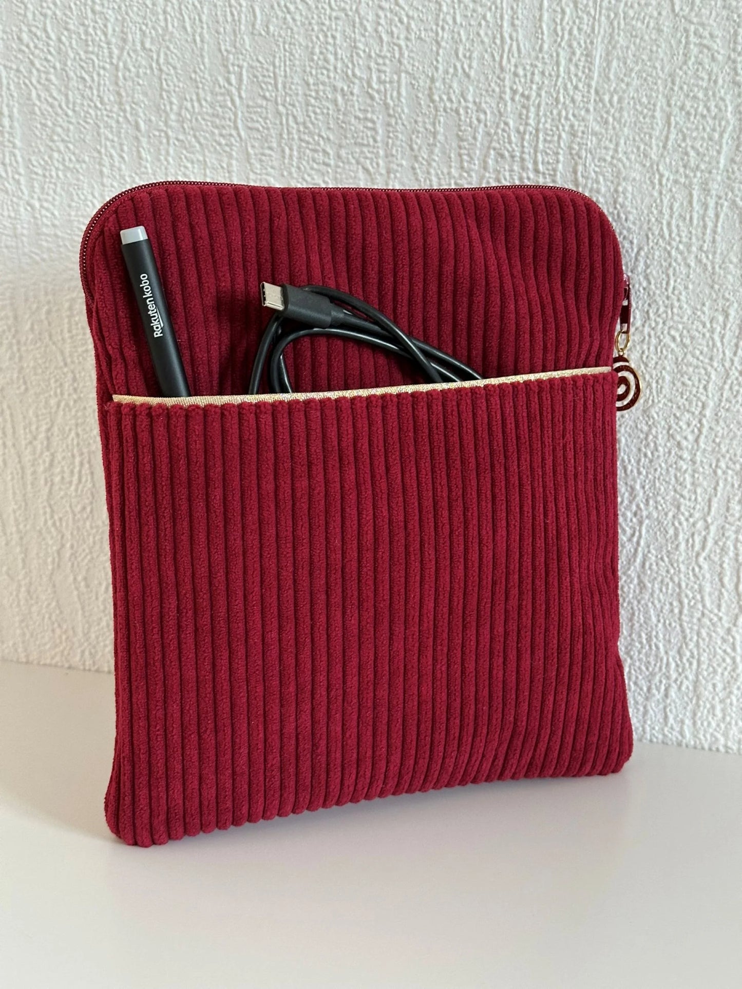 La pochette liseuse en velours cotelé bordeaux, avec stylet et cable dans la poche avant.