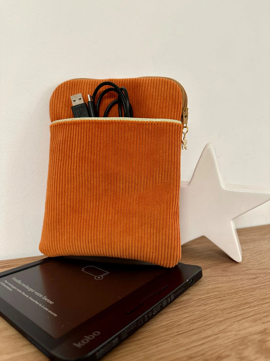 La pochette liseuse en velours côtelé orange, avec câble dans la poche avant.