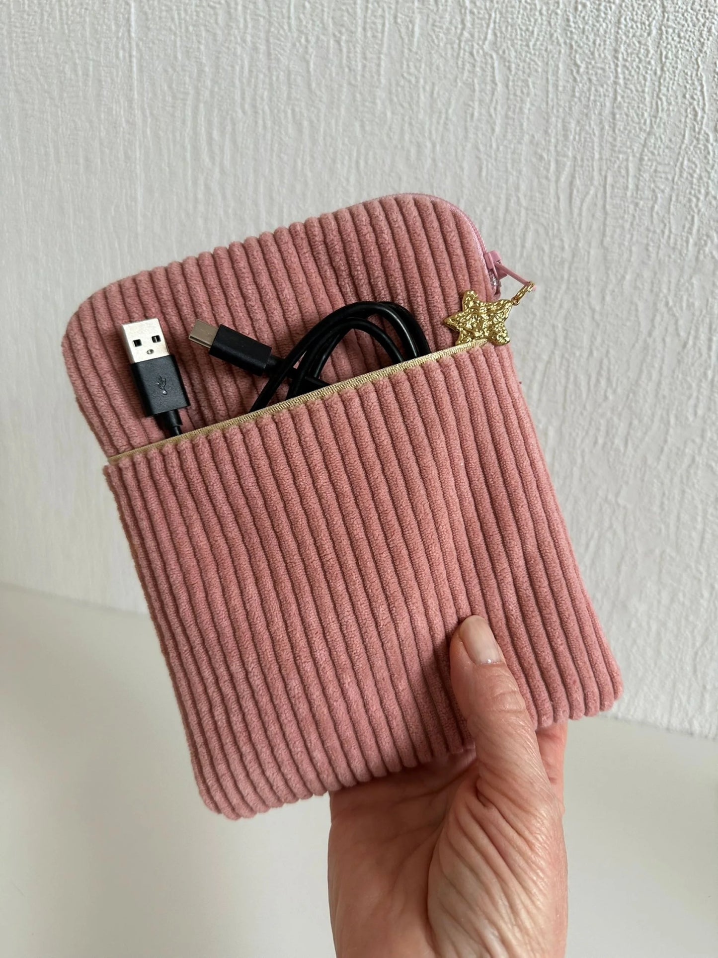 La pochette liseuse en velours cotelé rose blush tenue en main.