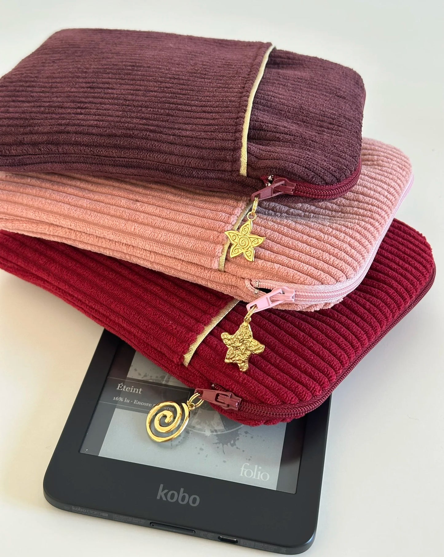 La pochette liseuse en velours prune, posée sur la prose blush et la bordeaux.