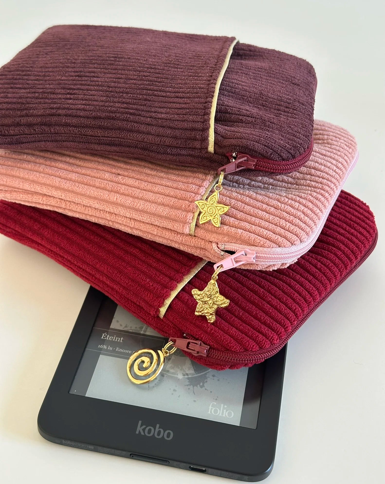 La pochette liseuse en velours prune, posée sur la prose blush et la bordeaux.