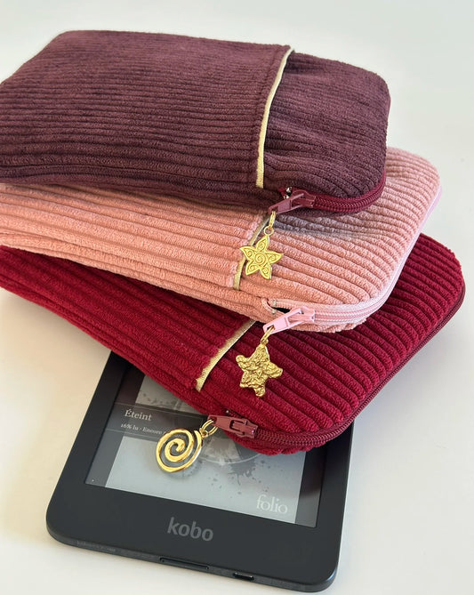 La pochette liseuse en velours prune, posée sur la prose blush et la bordeaux.