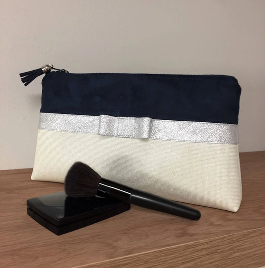 La pochette à maquillage bleu marine et blanc à noeud argenté.
