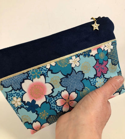La pochette à maquillage bleu marine en tissu japonais fleuri turquoise tenue en main.